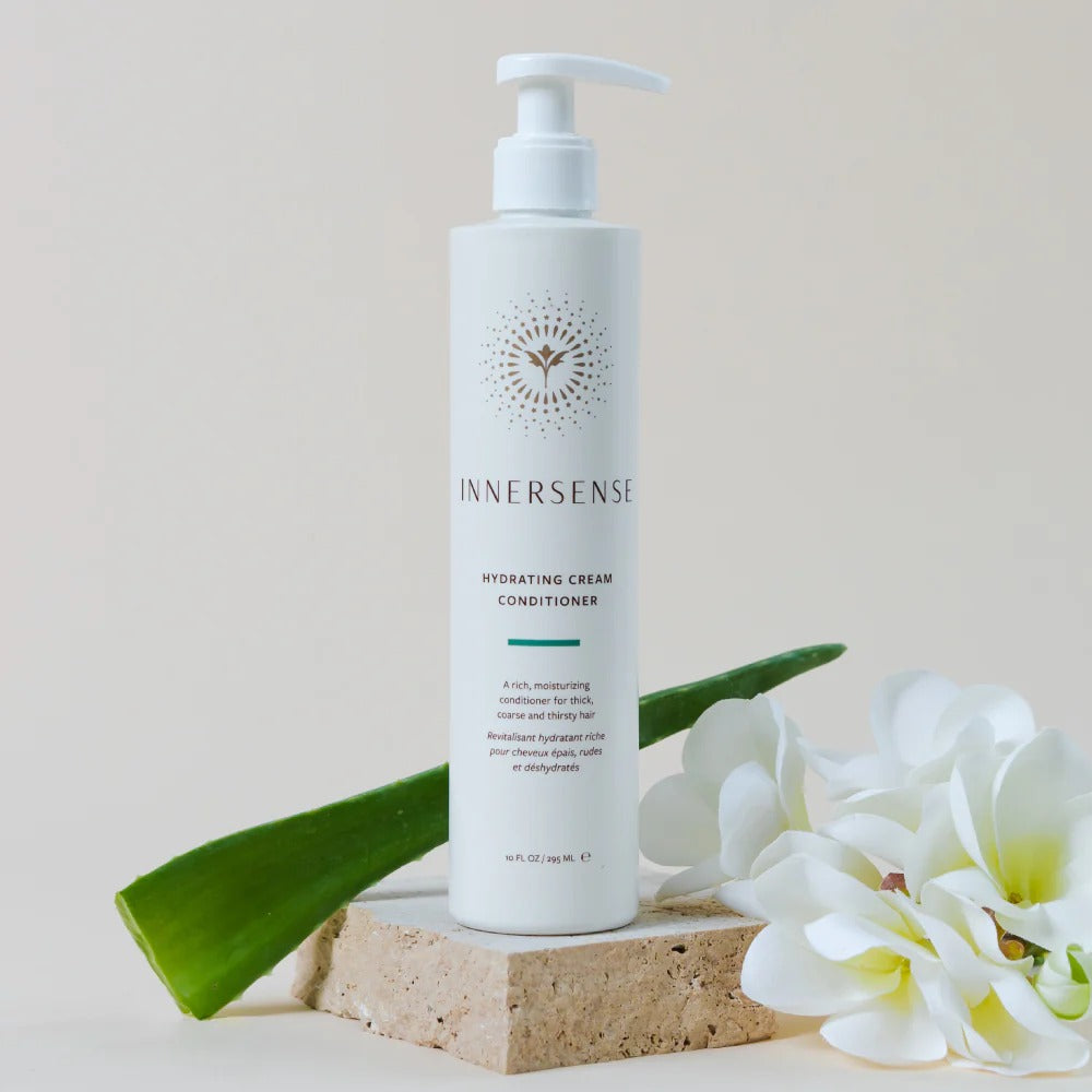 White Innersense Hydrating Cream Conditioner pump bottle on a stone block with aloe vera and white flowers.
