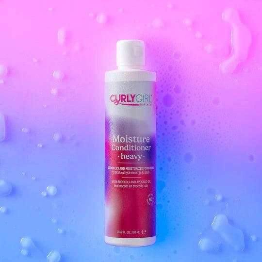 Curly Girl Movement Moisture Conditioner Heavy, 250ml white bottle with pink and purple label, on a wet blue and pink surface.