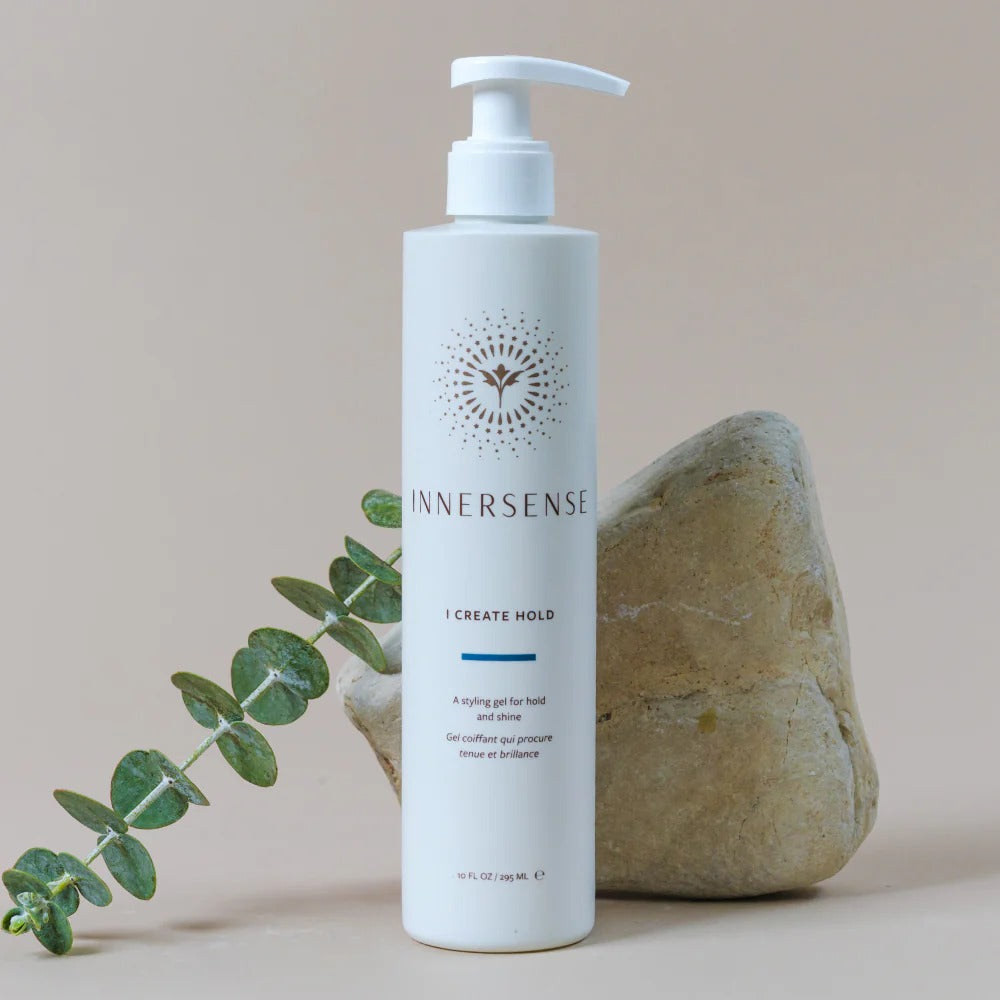 White Innersense I Create Hold styling gel bottle with pump, next to a rock and eucalyptus branch.