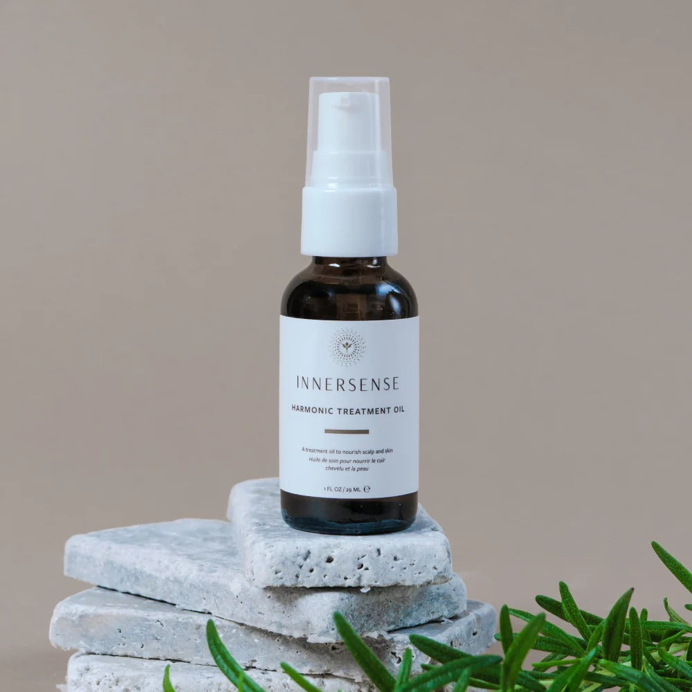 Innersense Harmonic Treatment Oil in a small amber bottle with a white pump, on stacked grey stones.