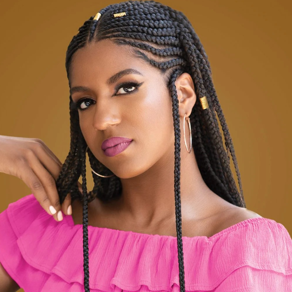 Woman with neat, long black box braids with gold cuffs, wearing a pink off-the-shoulder top and hoop earrings.