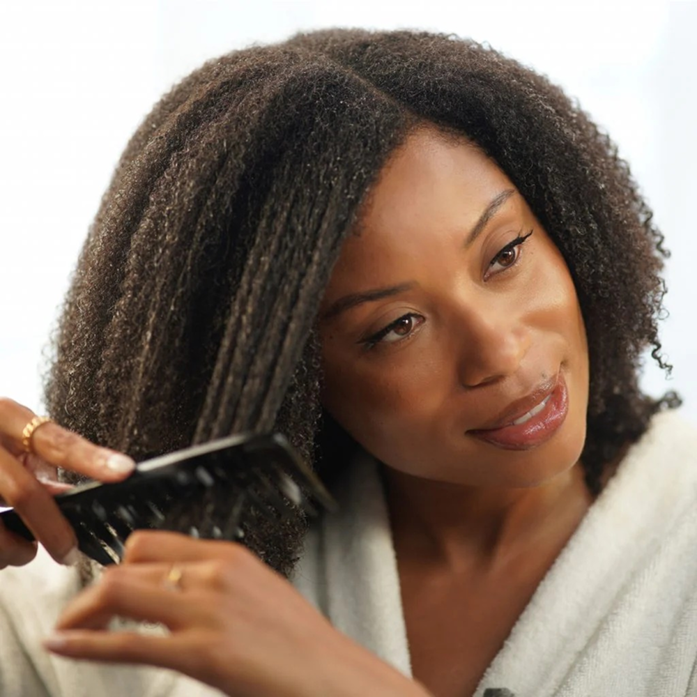 Woman with dark, curly hair combing through a section with a black wide-tooth comb.