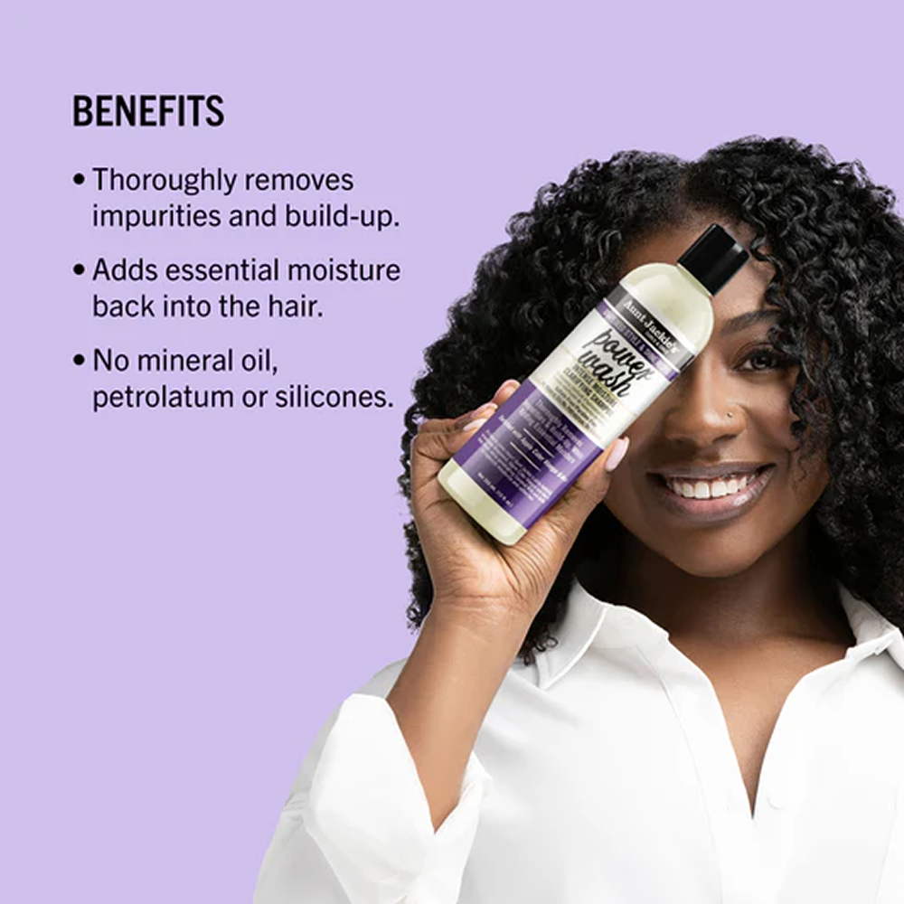 Smiling woman holding Aunt Jackie's Grapeseed Power Wash shampoo, a white bottle with purple label.