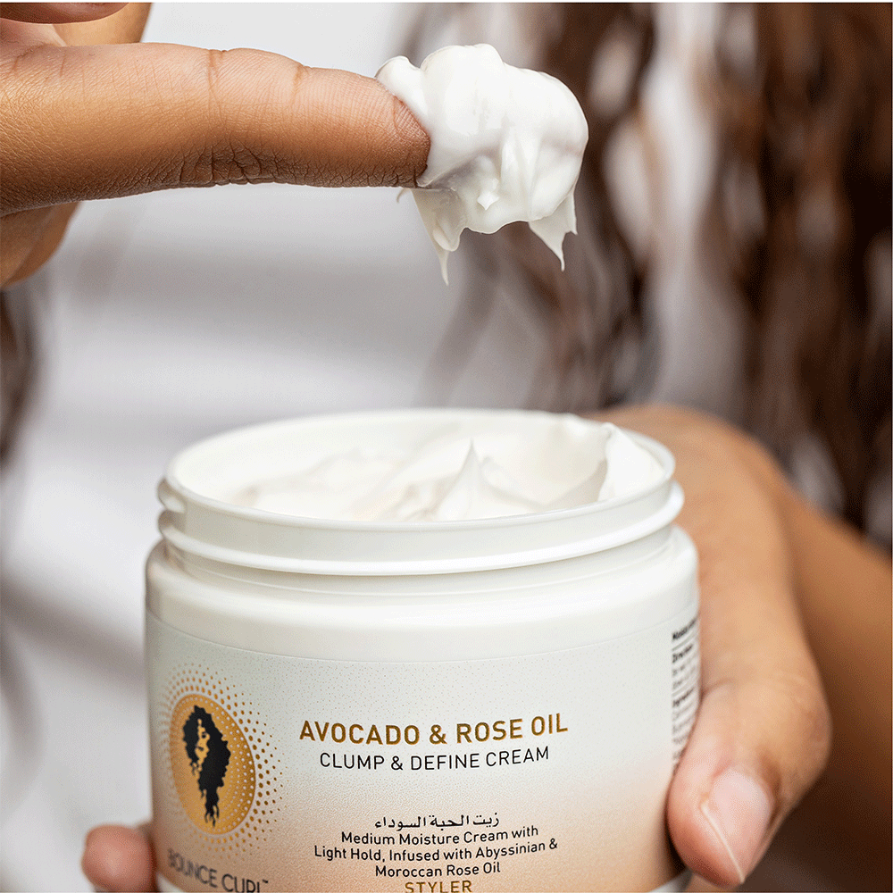 Hand dipping a finger into a white jar of Bounce Curl Avocado & Rose Oil Clump & Define Cream.