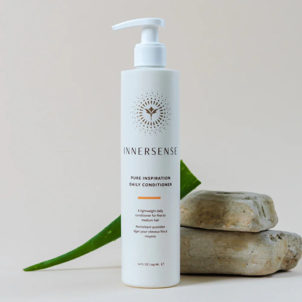 White Innersense Pure Inspiration Daily Conditioner bottle with a pump, aloe leaf, and two stones.