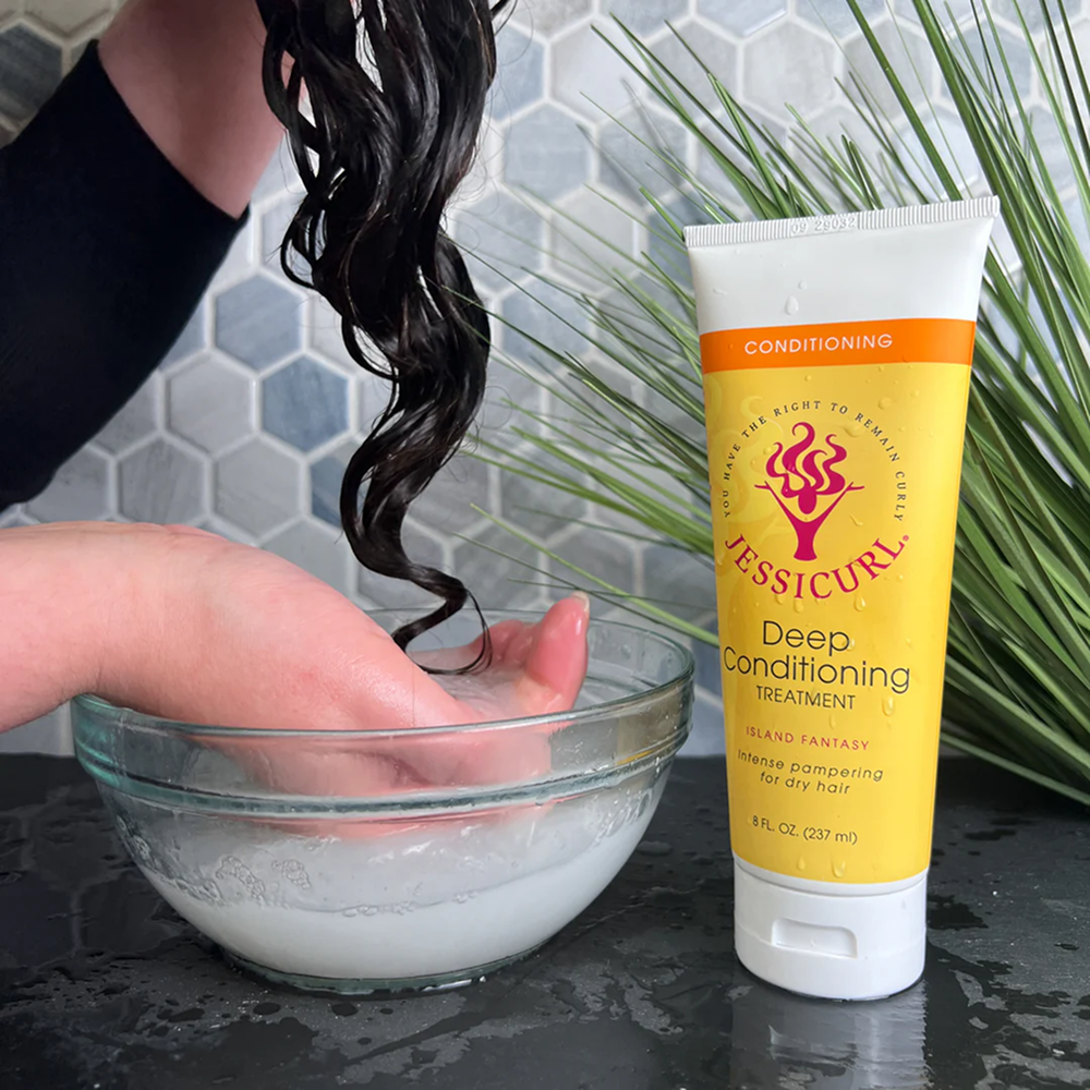 Jessicurl Deep Conditioning Treatment in a yellow tube next to a hand rinsing dark, wet curly hair in a glass bowl.