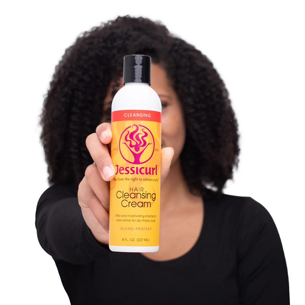 Woman holding a white Jessicurl Hair Cleansing Cream bottle with a yellow and red label.