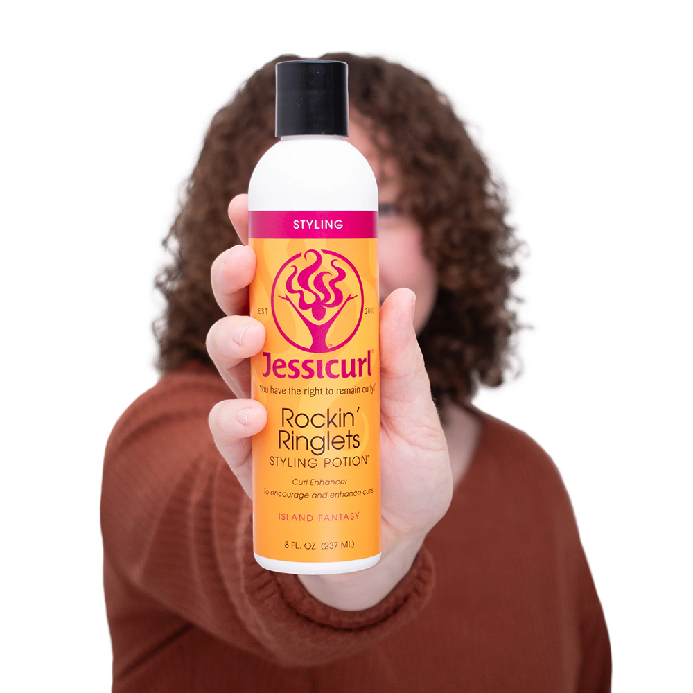 Hand holding a white Jessicurl Rockin' Ringlets Styling Potion bottle with an orange and pink label.