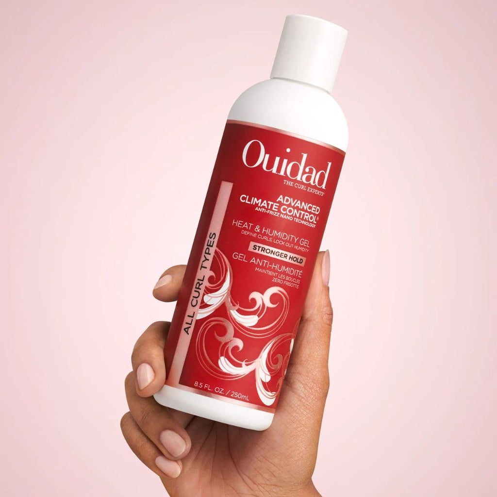 Hand holding a white Ouidad Advanced Climate Control Heat & Humidity Gel 250ml bottle with a red label.