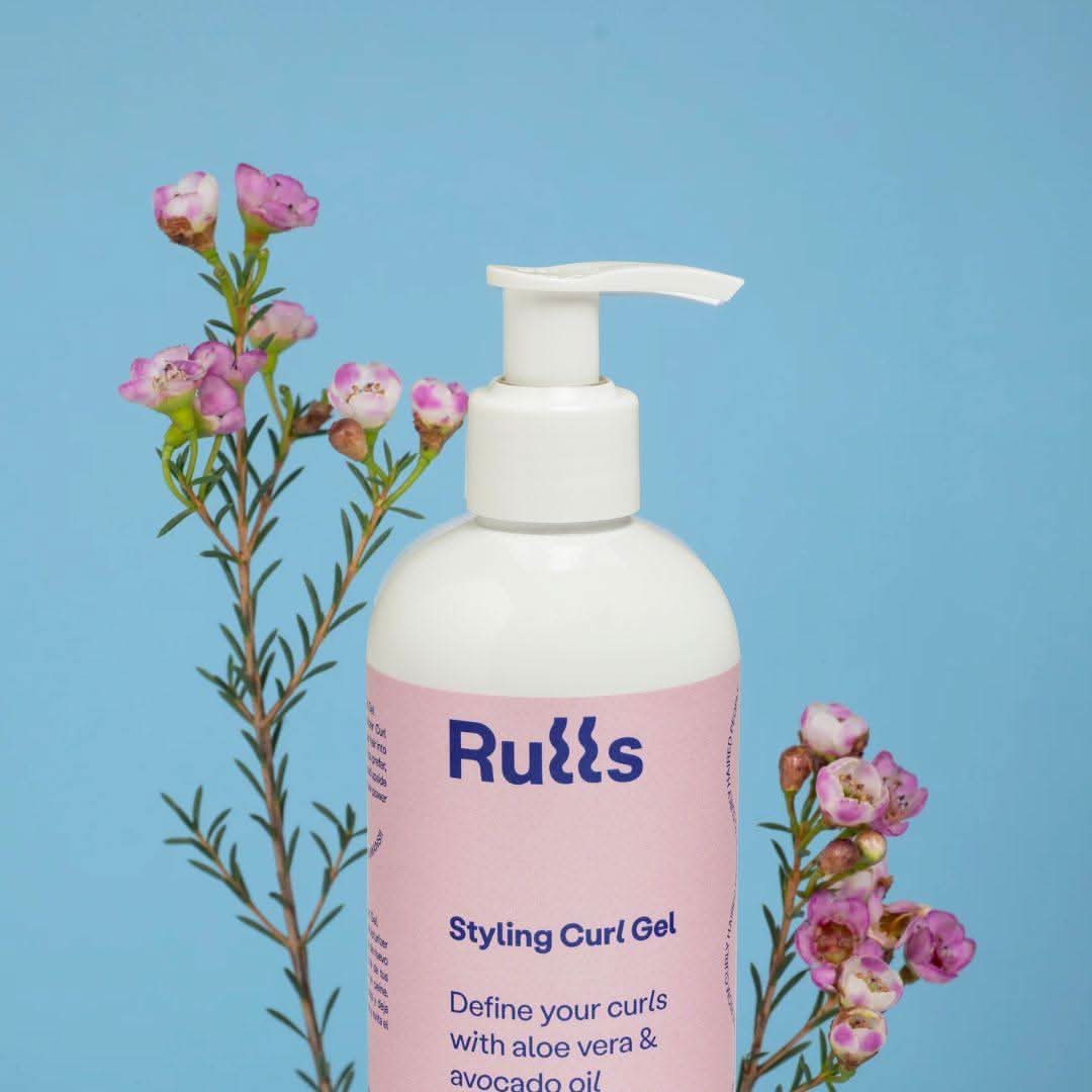 White Rulls Styling Curl Gel pump bottle with pink label, flanked by pink flowering branches.