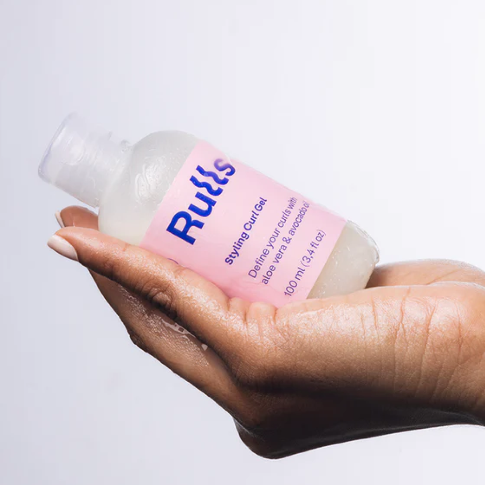 Hand holding a clear Rulls Styling Curl Gel bottle with a pink label.