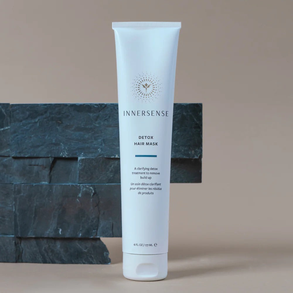 White Innersense Detox Hair Mask tube with gold logo, 6 fl oz, on a beige background with dark stone accents.