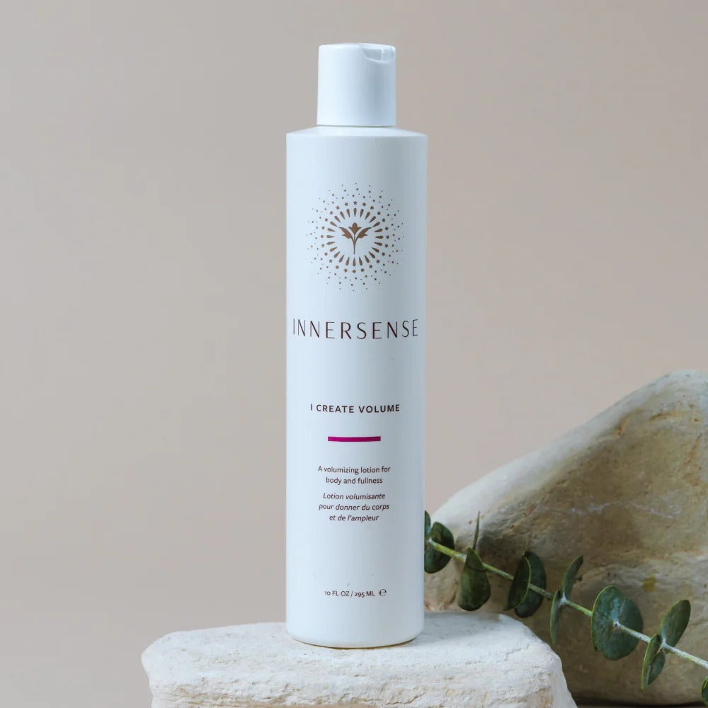 White Innersense I Create Volume lotion bottle with gold sunburst logo, on a light stone with eucalyptus.