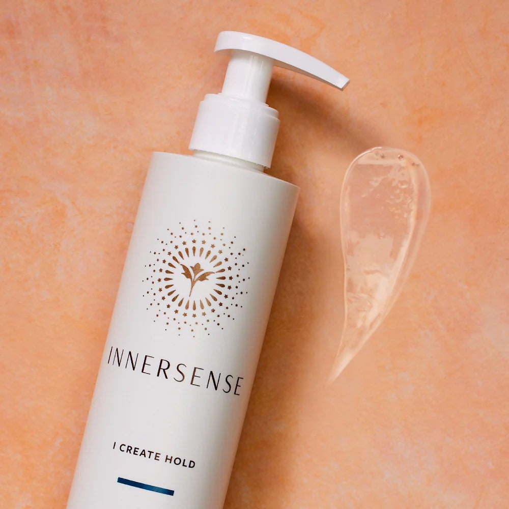 White Innersense I Create Hold pump bottle with a clear gel swatch on a peach background.