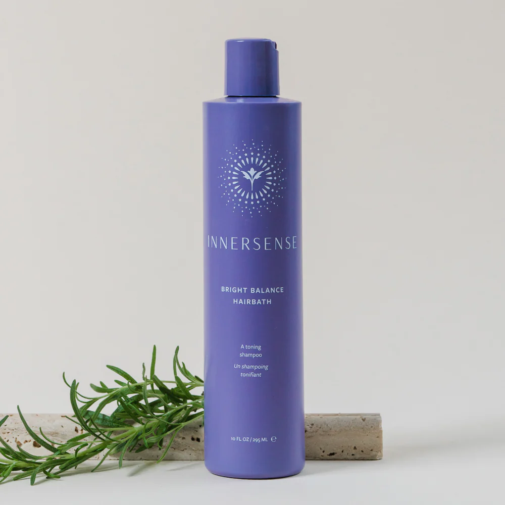Innersense Bright Balance Hairbath, a 10 fl oz purple shampoo bottle with a white sunburst logo, next to rosemary sprigs.
