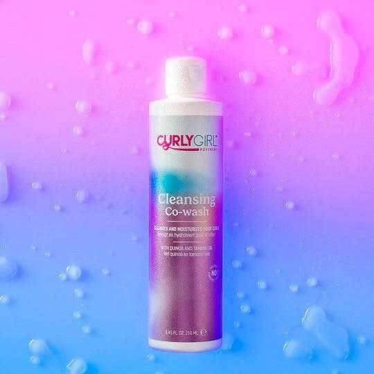 White bottle of Curly Girl Movement Cleansing Co-wash on a vibrant pink and blue background with water droplets.